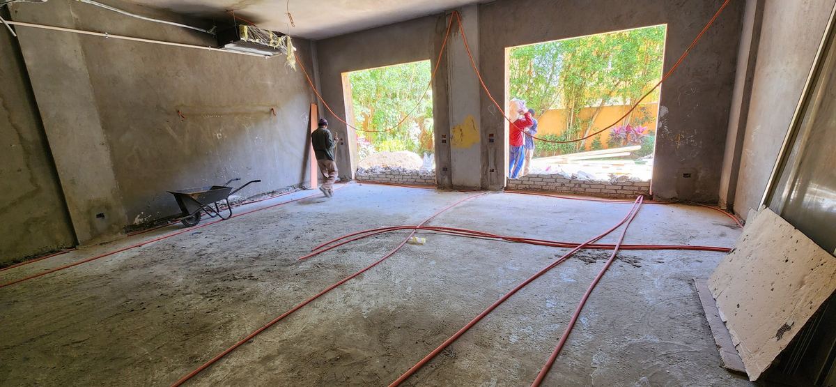 Before: L-Villa living room before finishing: bare plaster walls, exposed conduit and a wheelbarrow