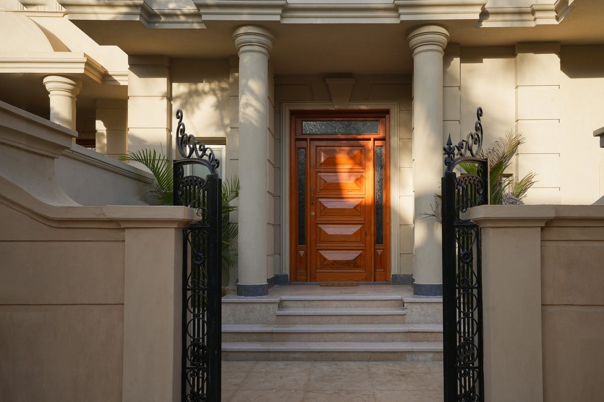 L-Villa entrance: stone columns, iron gate and a solid timber front door