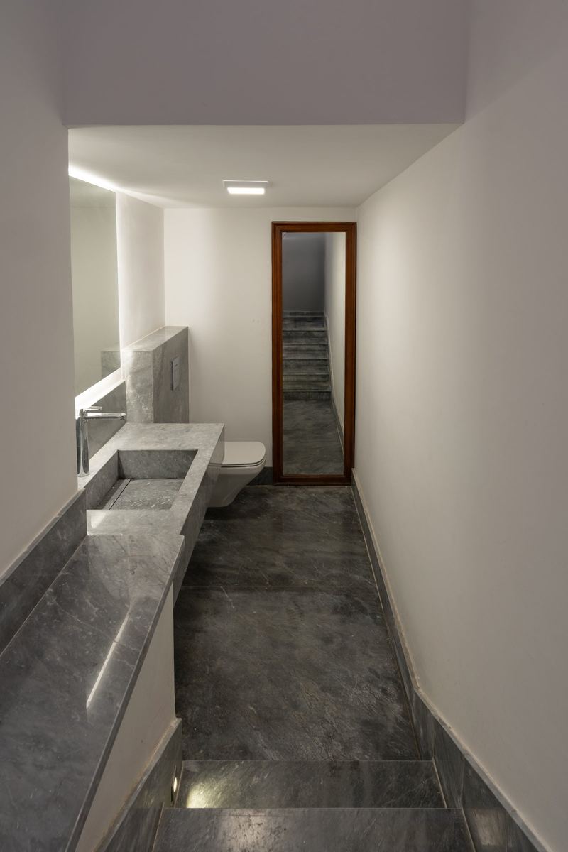 M-Villa bathroom under the stairs: long grey marble vanity, marble floor and a mirror at the end
