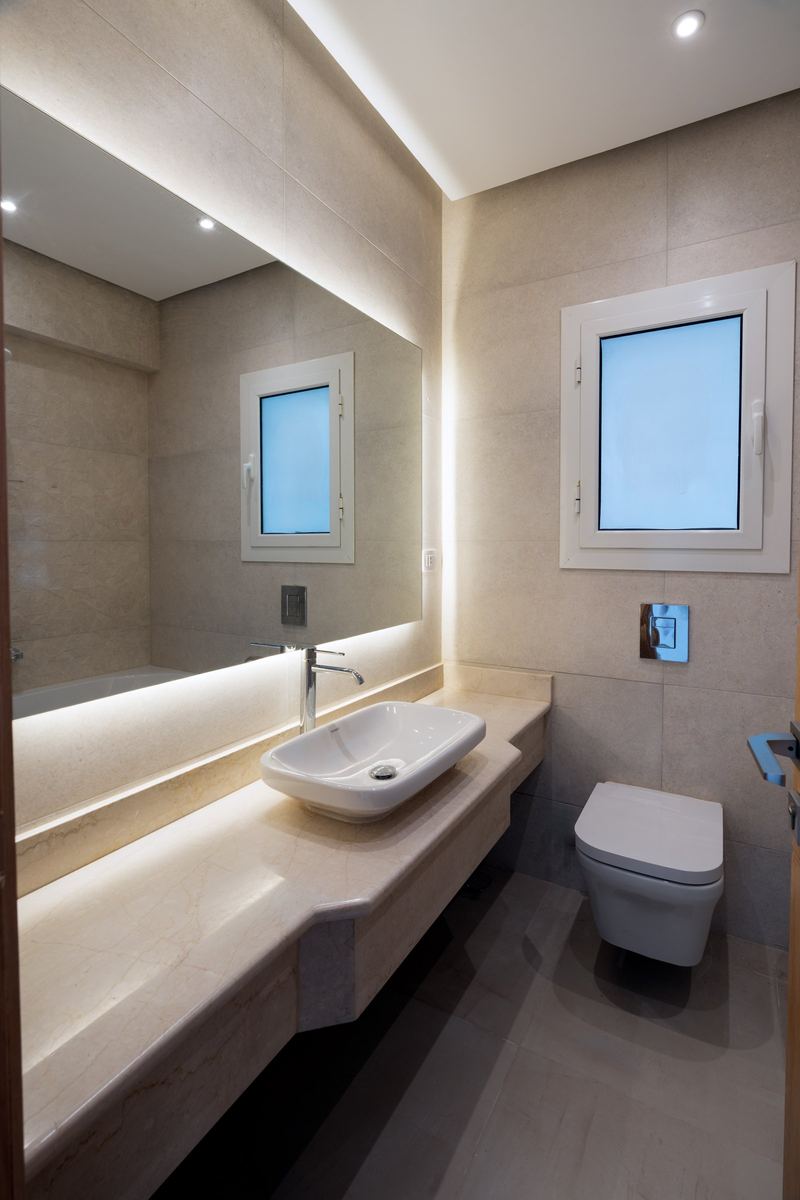 M-Villa guest bathroom: backlit mirror, stone vanity with a vessel basin and a wall-hung toilet