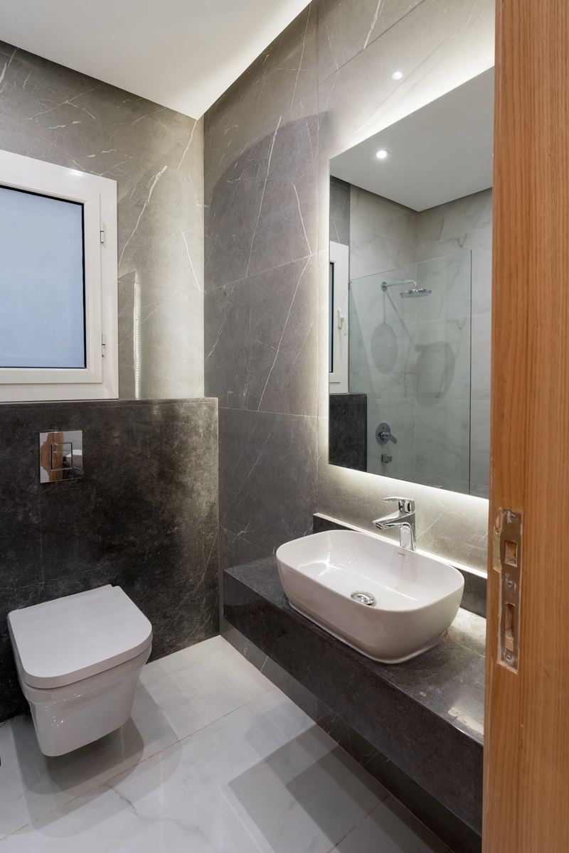 M-Villa bathroom: grey marble, backlit mirror, vessel basin and a glass shower