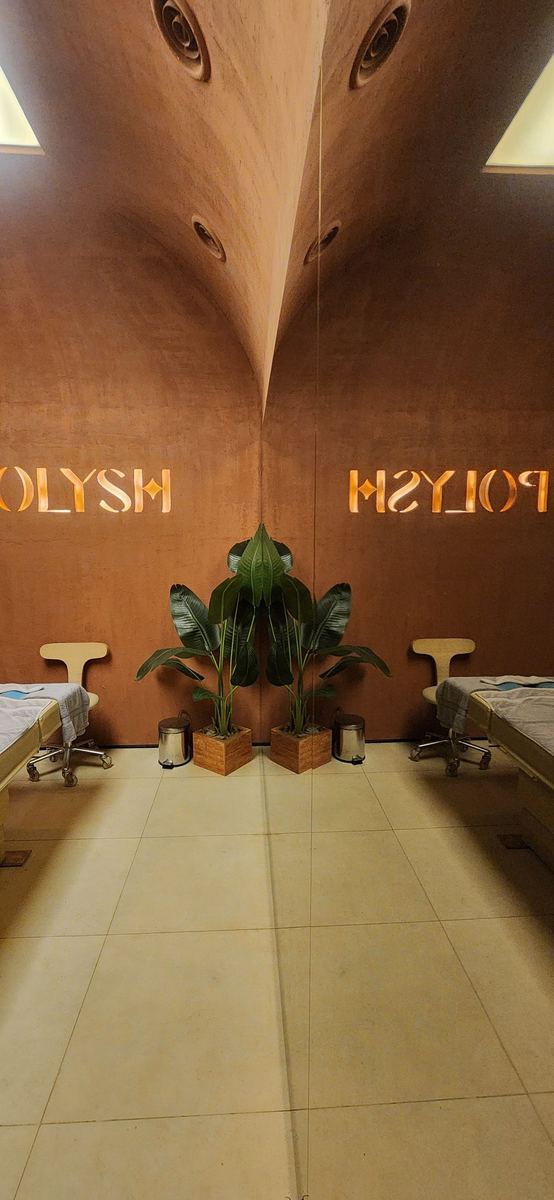 Polysh massage room reflected in a mirror wall: vaulted terracotta ceiling, two beds and a plant