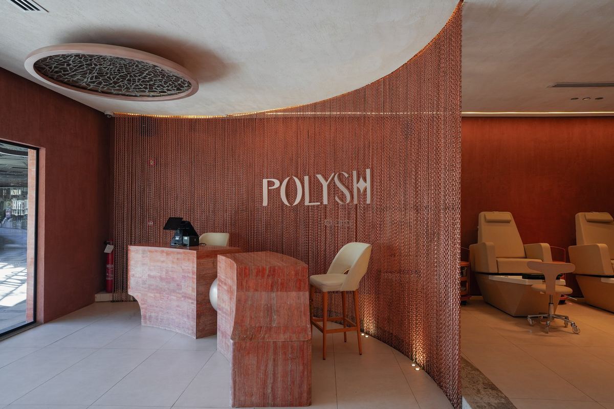 Polysh reception: curved terracotta desk in front of a copper chain curtain with the Polysh sign