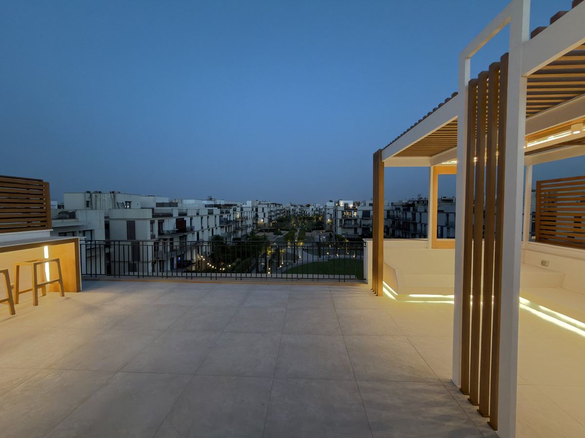 The whole terrace at blue hour as delivered: lit bar on the left, pergola on the right